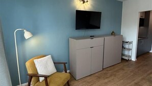 Ein Zimmer mit blauer Wand, Holzboden, einer Couch, einem an der Wand montierten Fernseher und einem Schrank.