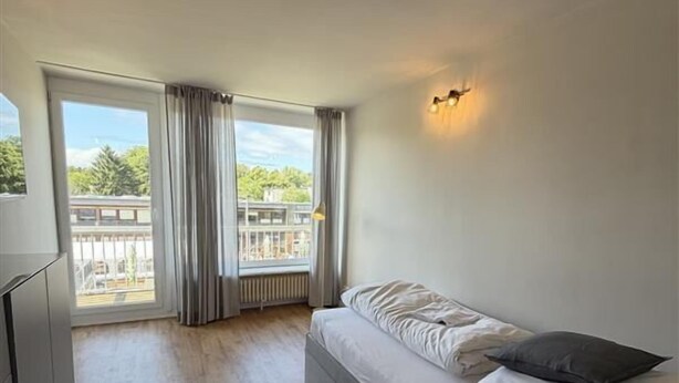 Ein modernes Zimmer mit einem Bett, einer hölzernen Bank, einem Heizkörper und einem Fenster mit Vorhängen.
