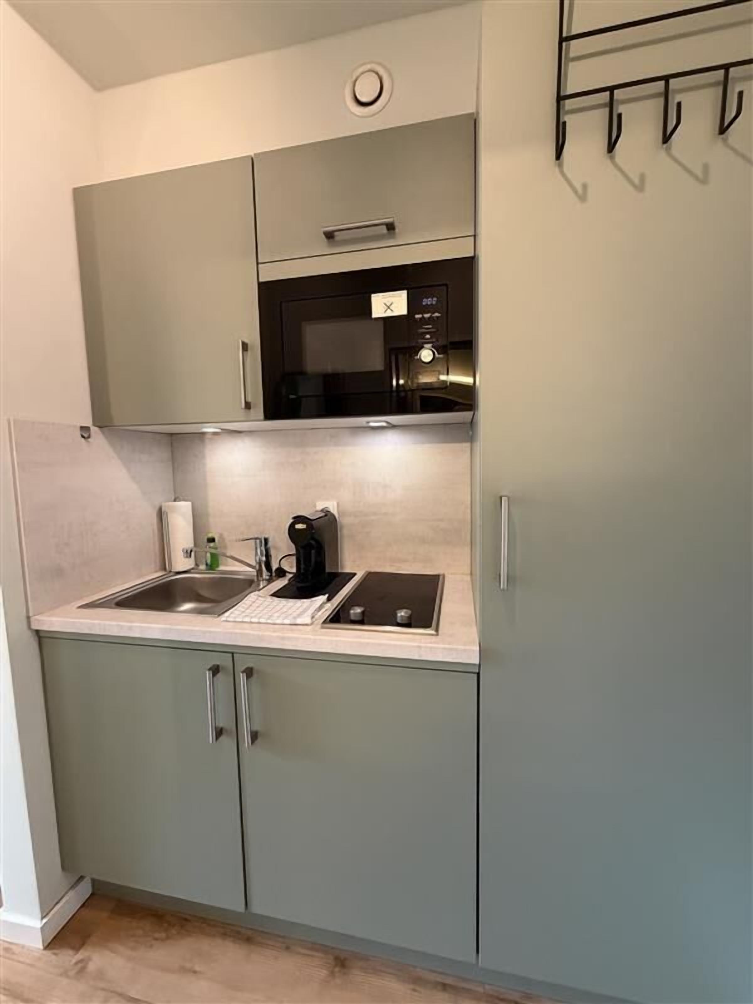 Una cocina compacta con microondas integrado, cafetera y lavamanos.