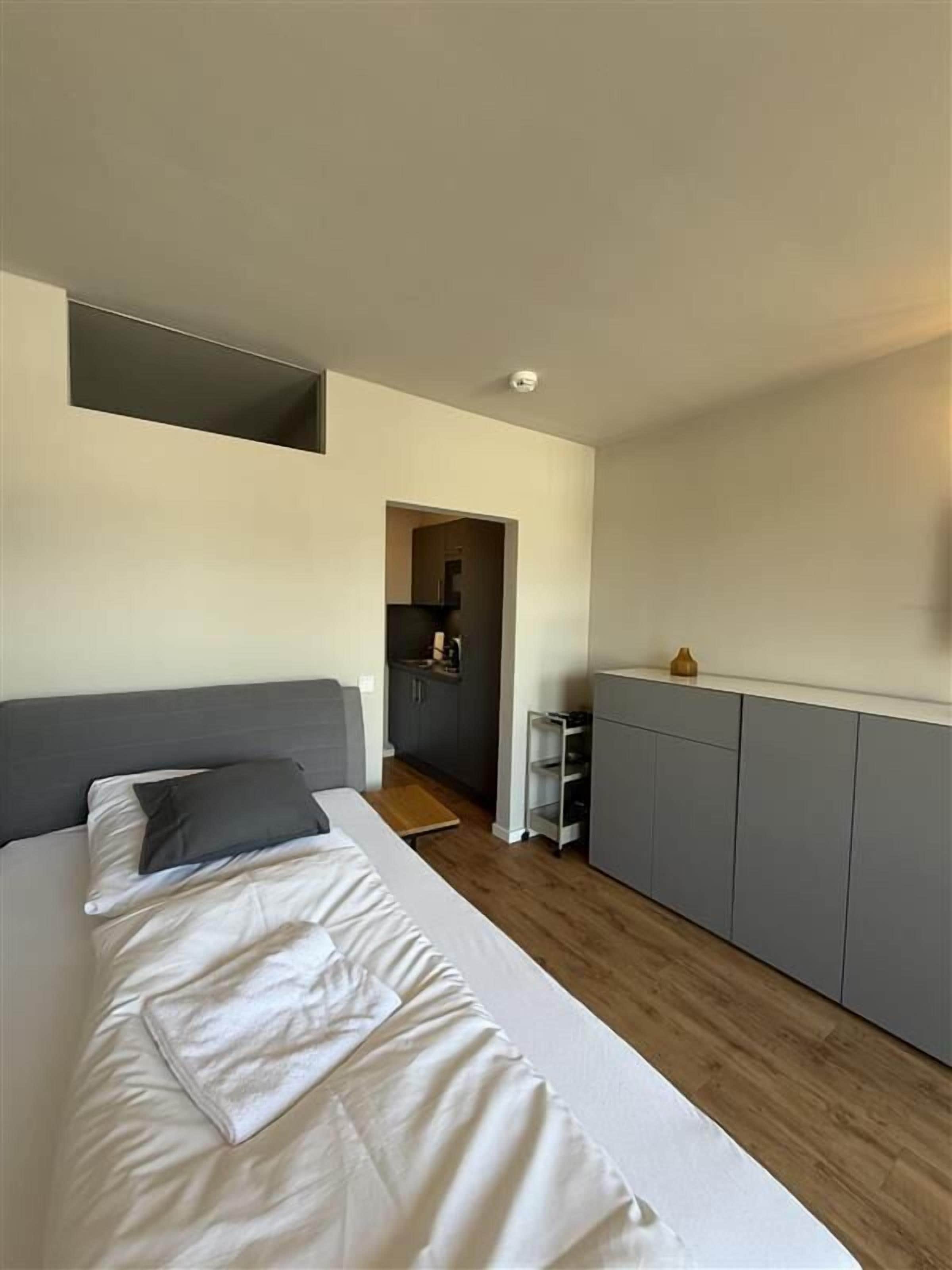 Un dormitorio con cama, una kitchenette pequeña y un armario gris.