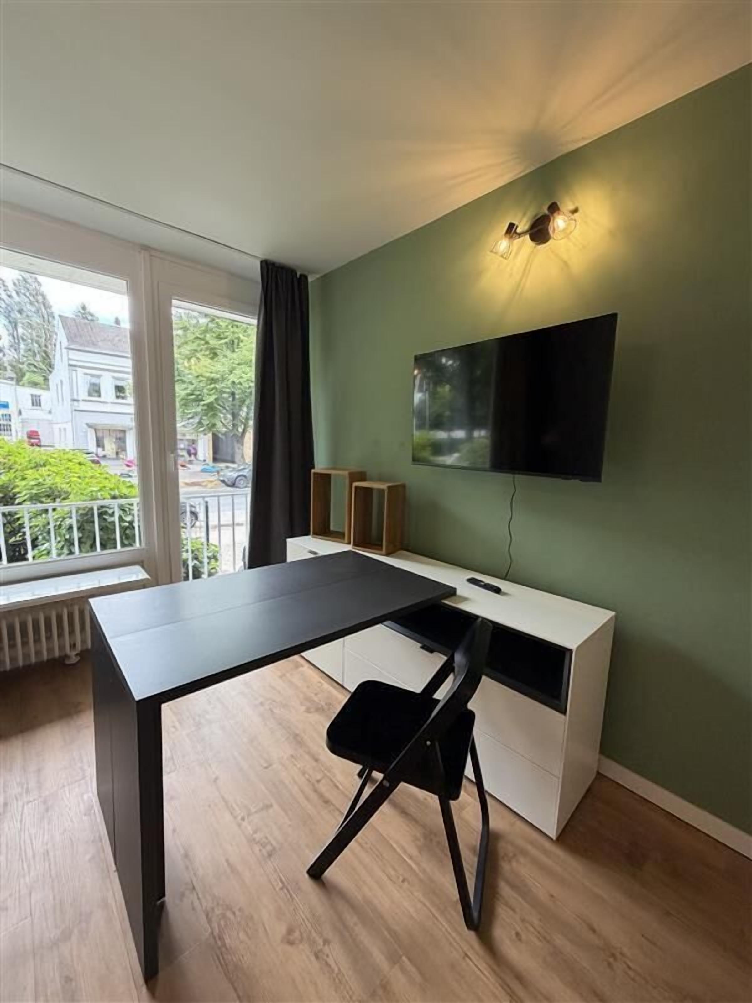 Ein Zimmer mit einem schwarzen Schreibtisch, einer weißen Kommode und einem Fernseher an der Wand.