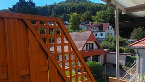 Ein Balkon mit einem hölzernen Gitter, einem Blumentopf und Blick auf Häuser und Bäume.