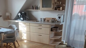 Eine kompakte Küche mit Kaffeemaschine, einem Esstisch mit Stühlen und einem großen Fenster mit transparenten Vorhängen.