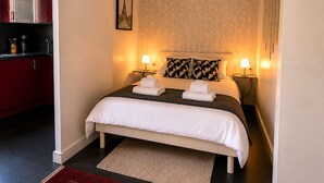 Ein Hotelzimmer mit einem Bett, zwei Nachttischlampen, einer Wand mit Muster, einem gerahmten Bild und einer roten Küchenzeile.