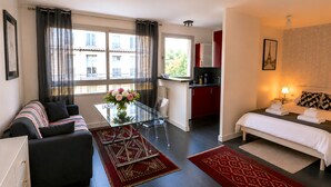 Ein modernes Hotelzimmer mit Sofa, einem Glastisch, einer Küchenzeile und einem Bett mit Handtüchern.