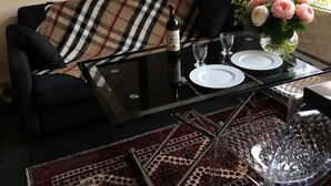 Ein Wohnzimmer mit einer Couch, einem Glastisch mit Weinflasche, Tellern und Besteck sowie einer dekorativen Vase mit Blumen.