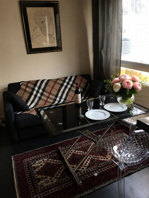 Ein Wohnzimmer mit einer Couch, einem Glastisch mit Weinflasche, Tellern und Besteck sowie einer dekorativen Vase mit Blumen.