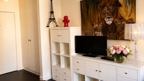 Ein modernes Wohnzimmer mit einer weißen Unterhaltungsanlage, einem Flachbildfernseher und Dekorationsobjekten, darunter ein Löwenbild, eine rote Skulptur und ein Modell des Eiffelturms.