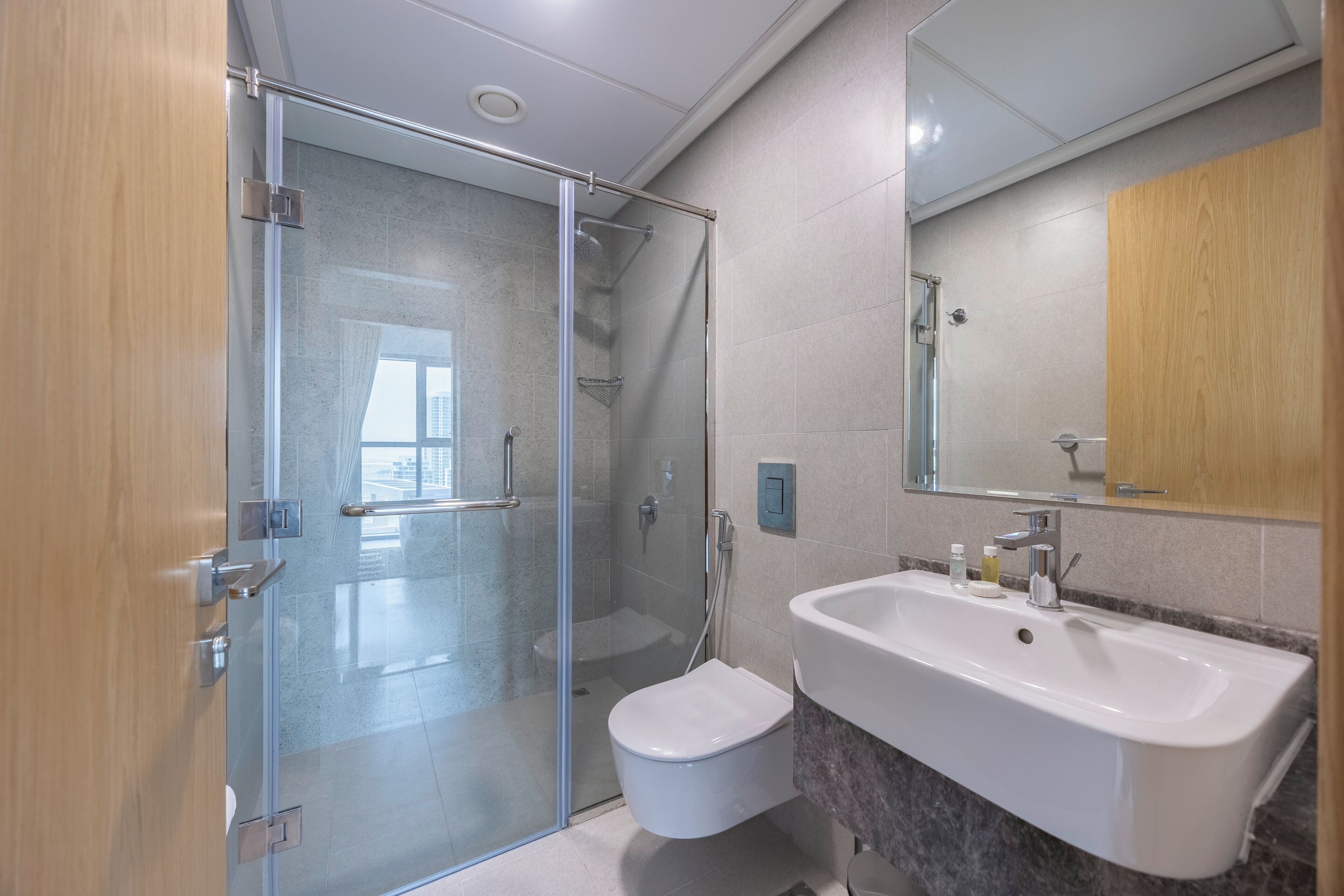 Un baño moderno con cabina de ducha de vidrio, inodoro blanco, un lavabo grande con encimera de mármol y un espejo sobre el lavabo.