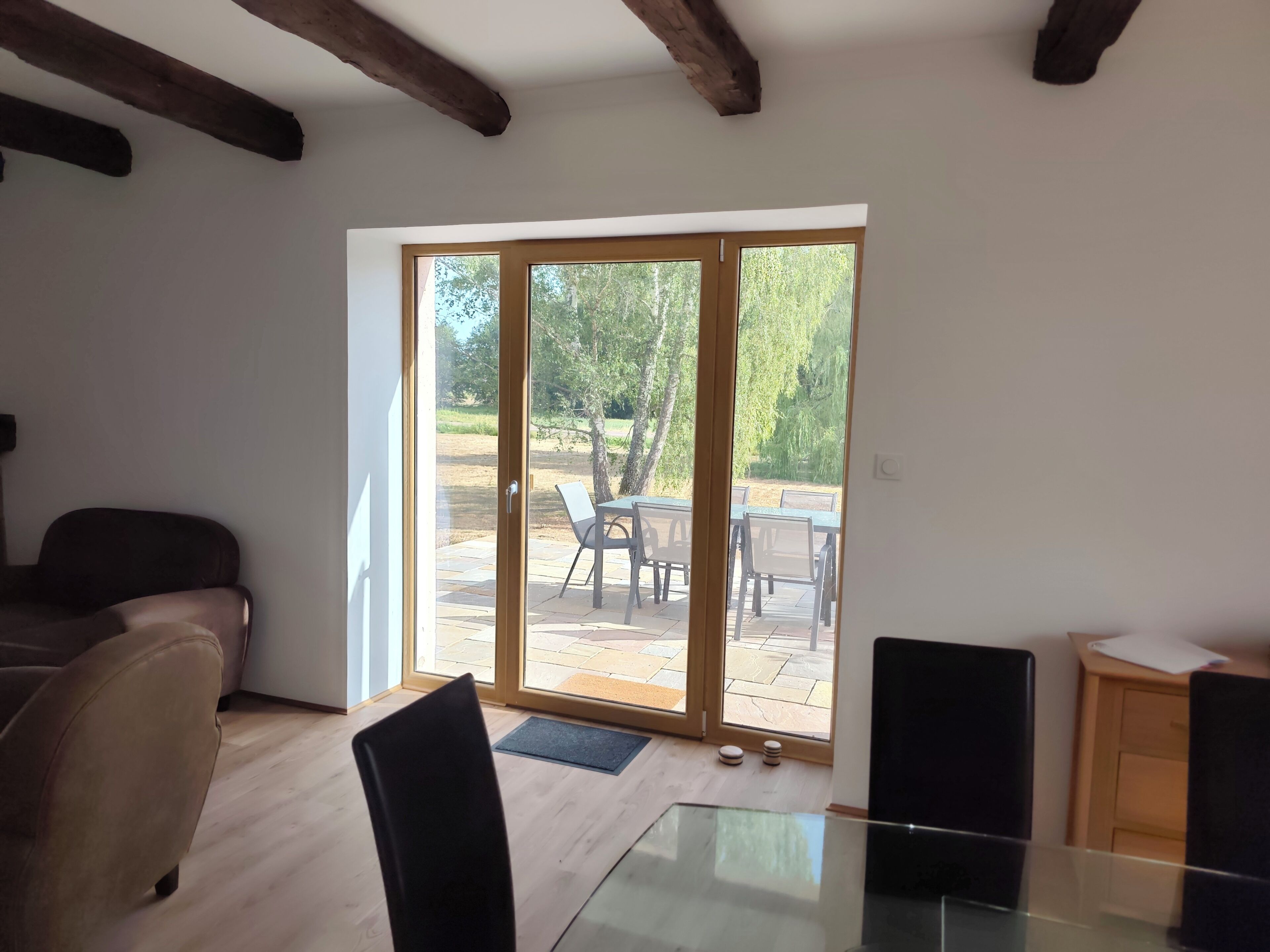 A room with a glass table, a sofa, and a sliding glass door leading to an outdoor patio with chairs and a table.