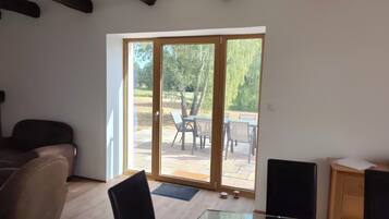 Een kamer met een glazen tafel, een bank en een glazen schuifdeur naar een terras met stoelen en een tafel.
