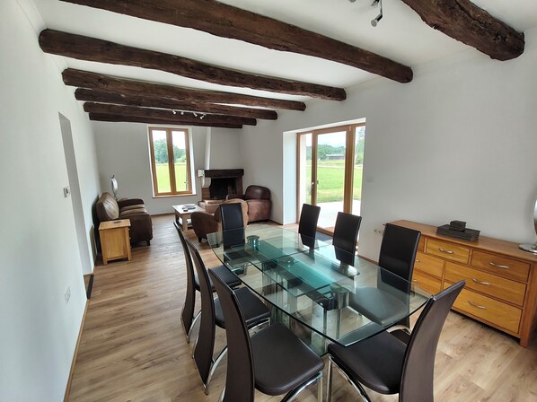 A spacious room with a glass-top dining table, wooden floor, and exposed wooden beams on the ceiling. - 3 double bedroom gite, each with private bathroom in a beautiful location. (Fiménil)