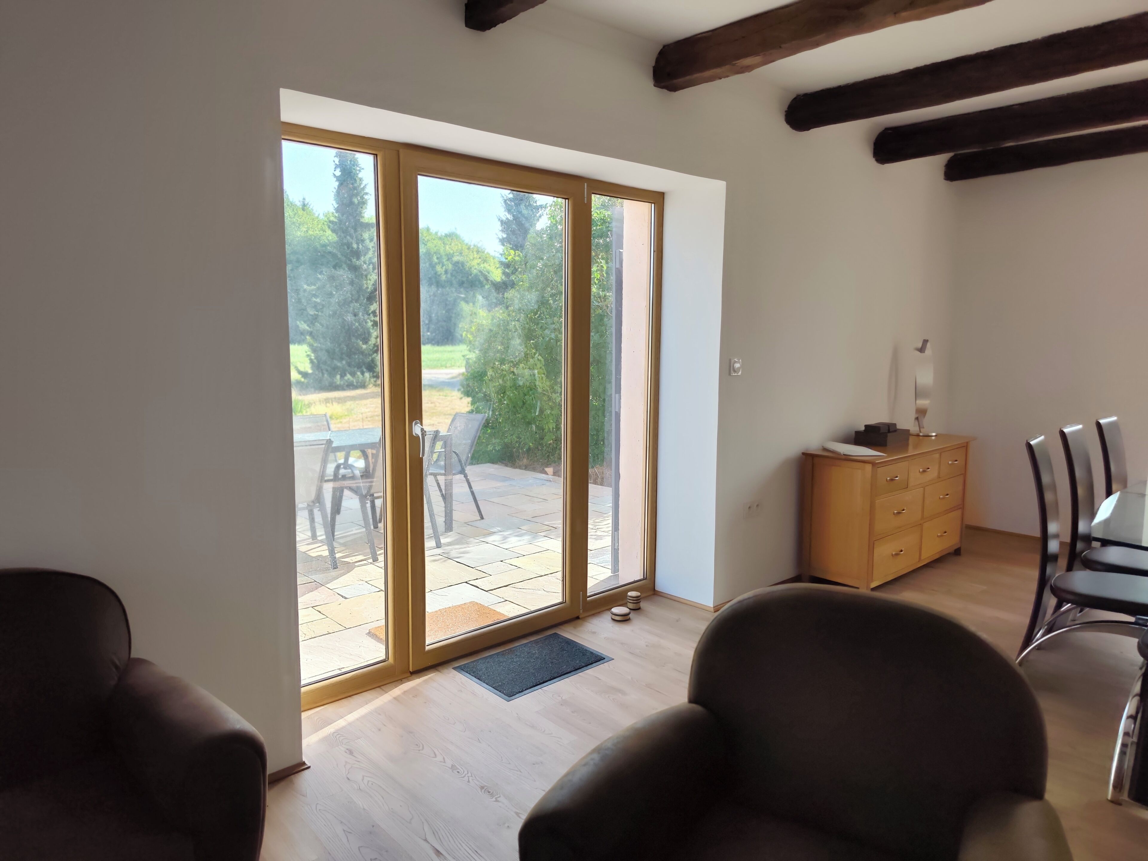 A room with a sliding glass door leading to an outdoor patio area, a wooden cabinet, and a dining table with chairs.