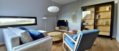 A modern living room with a sofa, a chair, a TV, a small table, and a bookshelf.