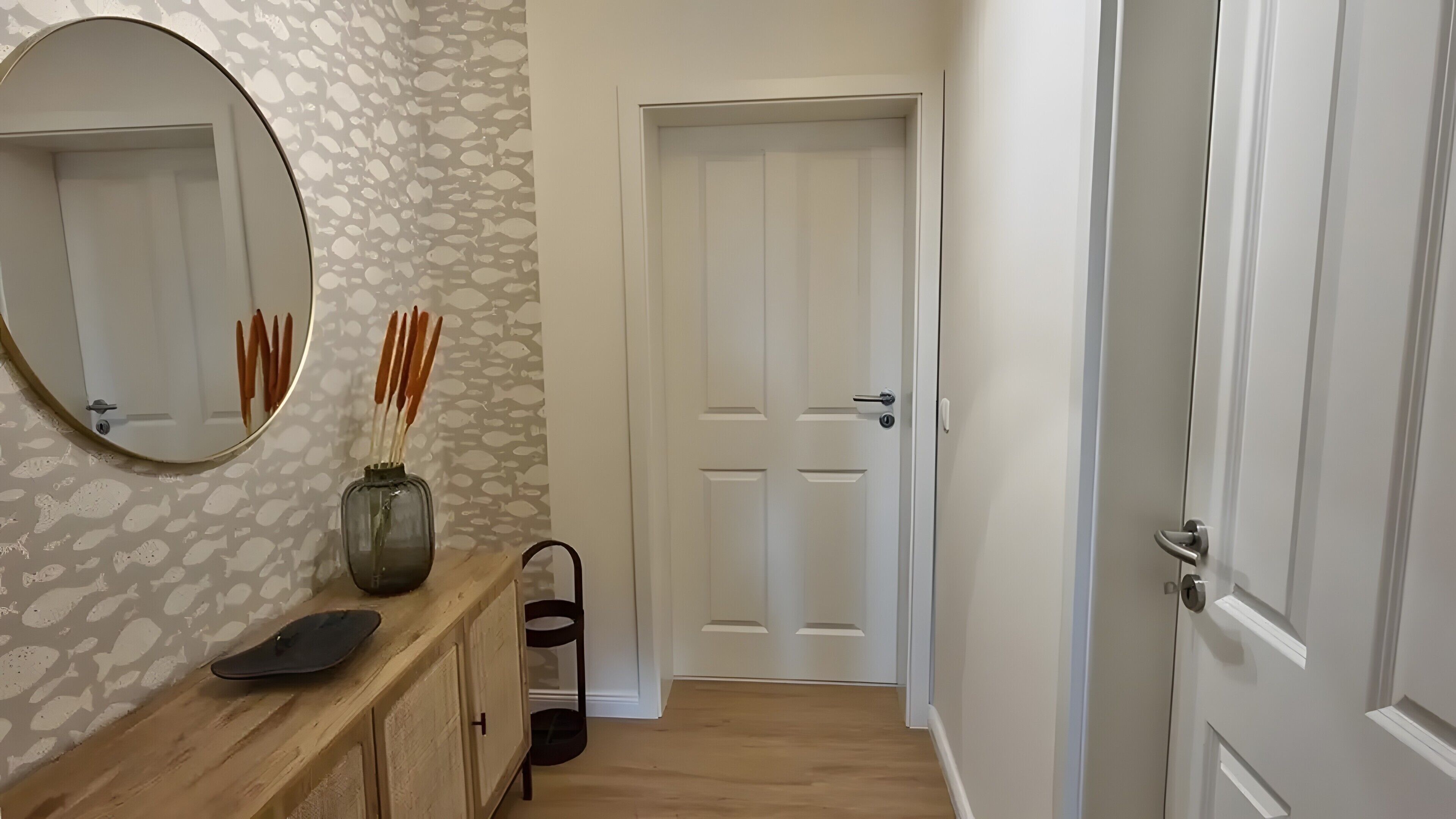 A hallway with a wooden counter, a mirror, a vase with sticks, and a door.