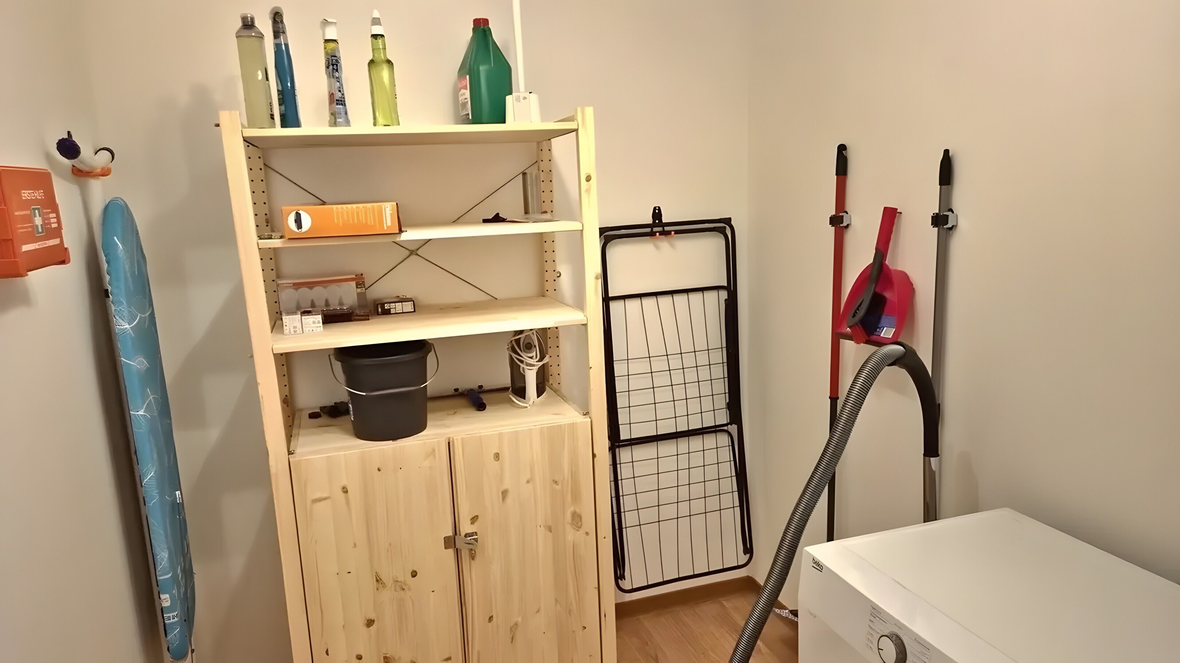 Une pièce avec un meuble en bois, des étagères remplies de bouteilles, un aspirateur et un présentoir à motifs en forme de quadrillage.
