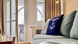 A room with a sofa, a table with a glass, and a view through a glass door. - Moderne Ferienwohnung mit Balkon in Sudostlage in Sellin (Sellin)
