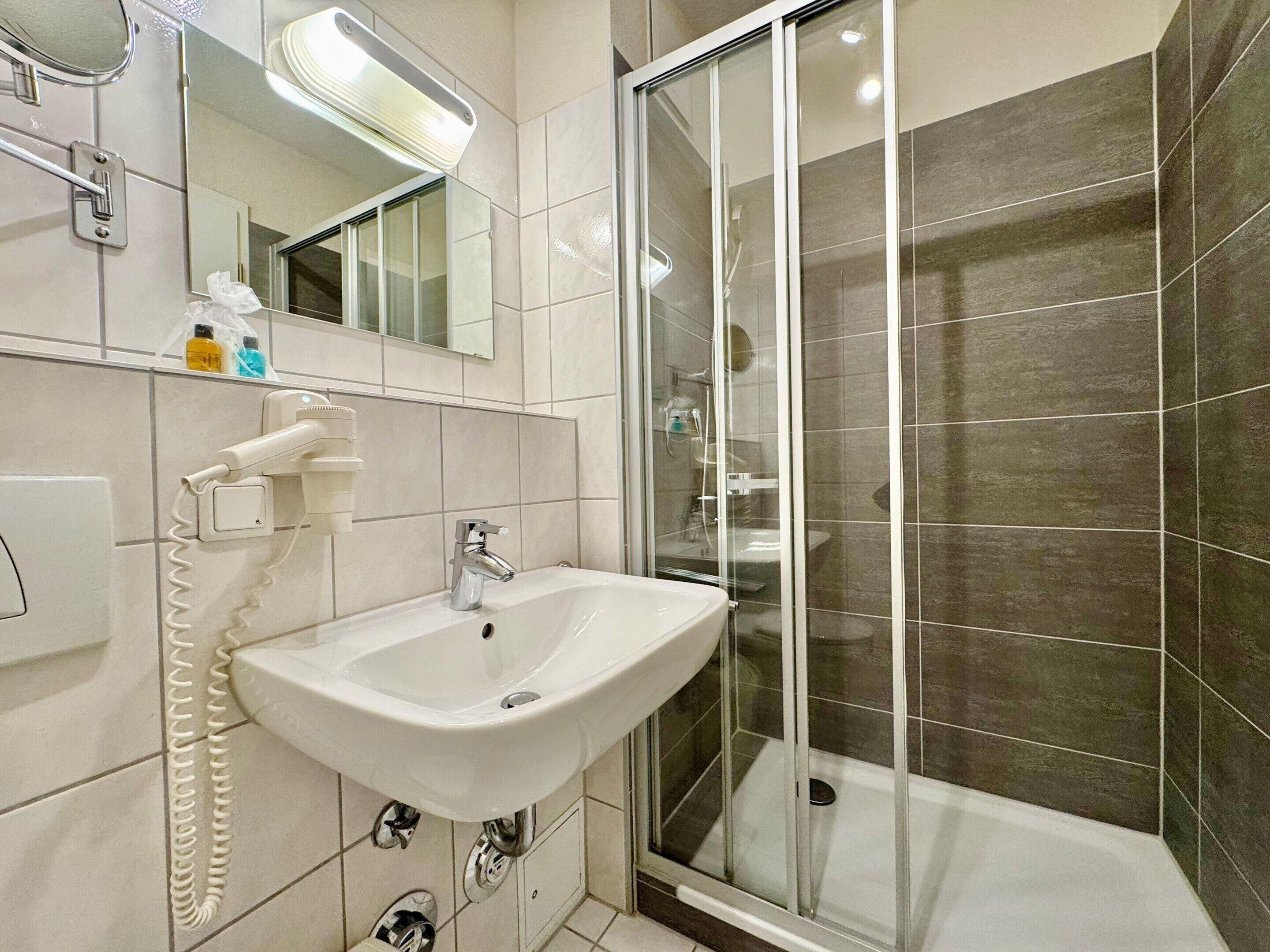 A bathroom with a white sink, a mirror, a shower with a glass door, and tiled walls.