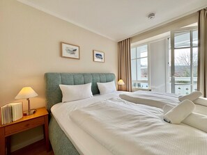 Ein Hotelzimmer mit zwei Betten, einem Nachttisch mit Lampe, einem Fenster mit Vorhängen und zwei gerahmten Bildern an der Wand.