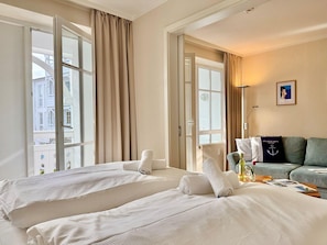 A hotel room with two beds, a sofa, a radiator, and a window with curtains. - Moderne Ferienwohnung mit Balkon in Sudostlage in Sellin (Sellin)