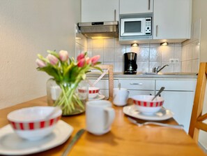 A kitchen with white cabinets, a microwave, a coffee maker, and a table set with bowls and a vase of flowers. - Moderne Ferienwohnung mit Balkon in Sudostlage in Sellin (Sellin)
