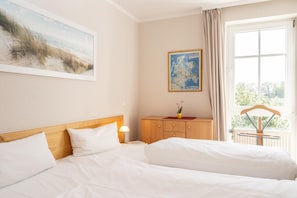 A hotel room with two beds, a wooden headboard, a nightstand with a lamp, a wooden dresser, a map on the wall, and a window with curtains. - Helle und Gemutliche Ferienwohnung mit Balkon im Seepark Sellin (Sellin)