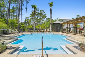 Ein Swimmingpool mit Liegestühlen und einer Pergola, umgeben von hohen Bäumen und einem Gebäude im Hintergrund.