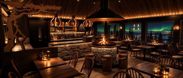 A restaurant with a stone fireplace, wooden tables, and chairs, and a view of the northern lights.