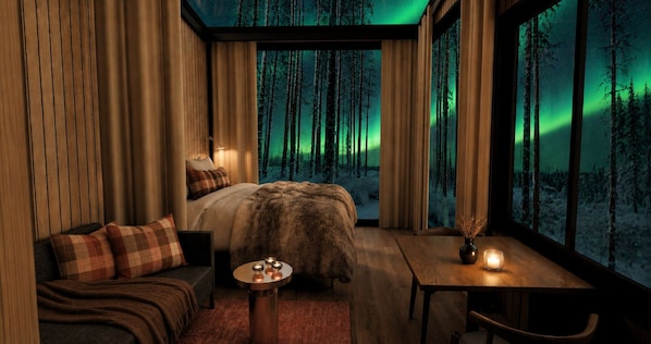 Una habitación acogedora con cama, sofá, una mesa con velas y vistas a un bosque a través de amplias ventanas.