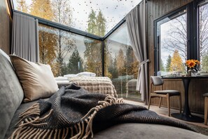 A modern bedroom with a glass ceiling, a cozy bed, a wooden desk, and a view of autumn trees. - Aava Glass Igloos (Rovaniemi)