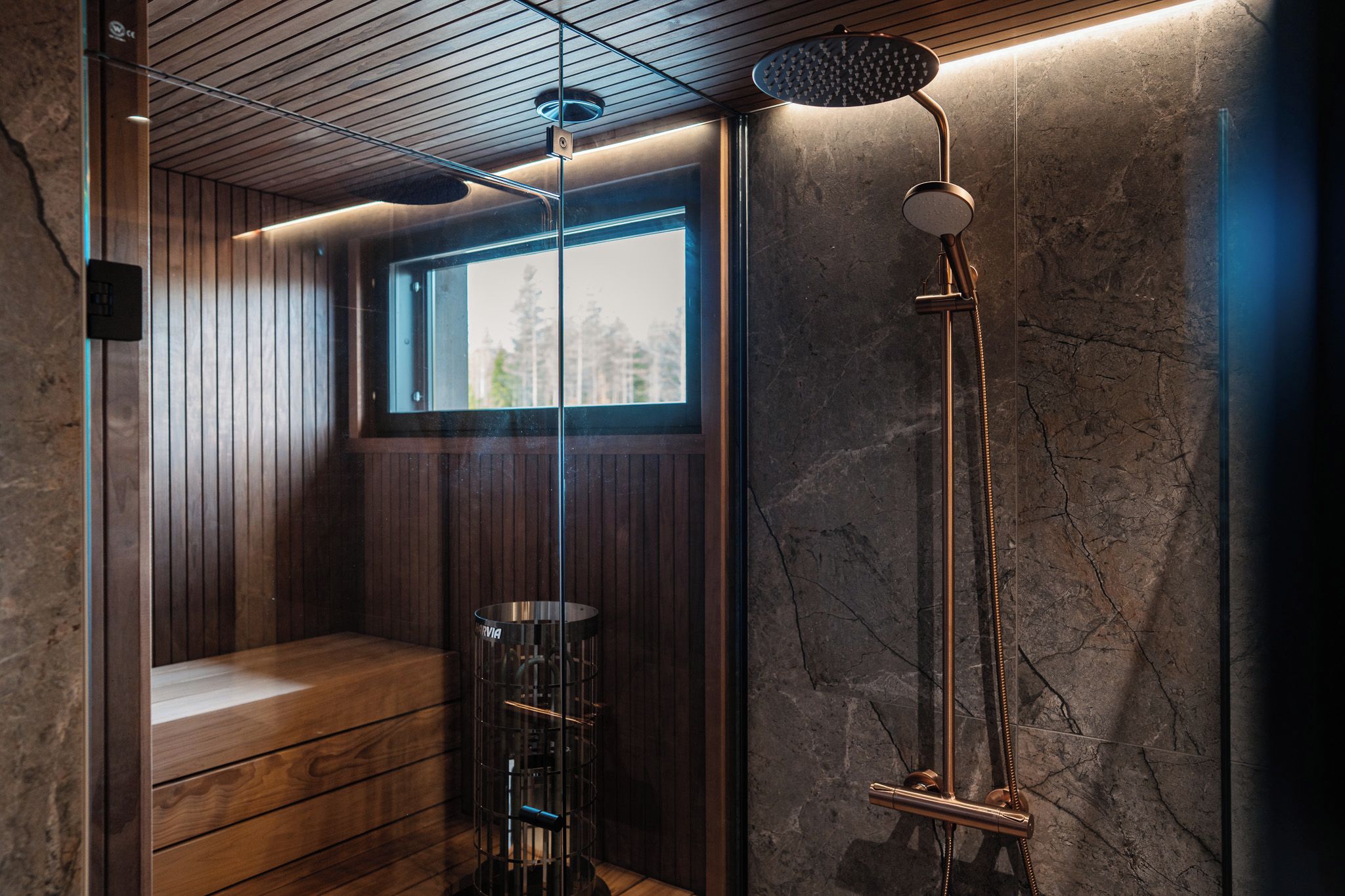 A modern bathroom with a wooden bench, a glass shower enclosure, and a stone wall.