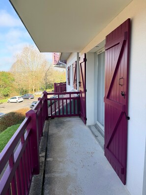 Ein Balkon mit Betonboden, roter Geländer und Blick auf geparkte Autos und Bäume.