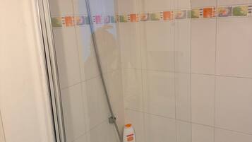 Eine Dusche mit Duschbrause, Seifenspender und Glastür.