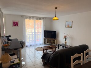 Ein Wohnzimmer mit Sofa, Fernseher, Couchtisch und einem Esstisch mit Stühlen.