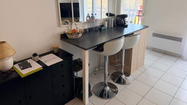 Uma cozinha com bancada preta, dois banquetes brancos, um espelho e uma janela com cortinas.