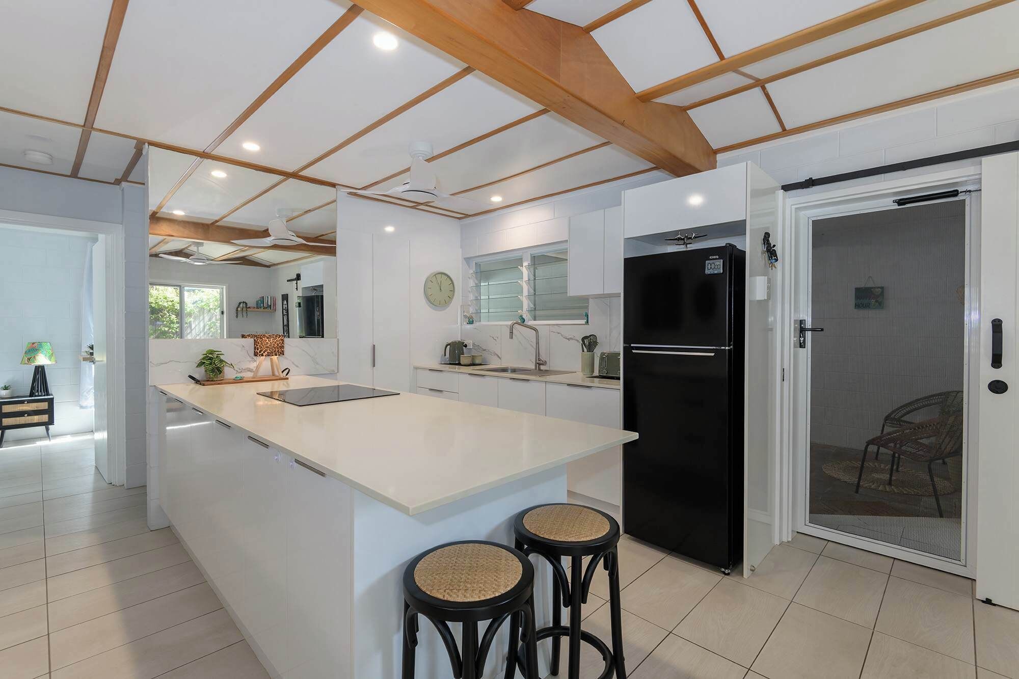 A modern kitchen with a central island, black refrigerator, and two stools.