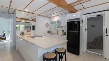 A modern kitchen with a central island, black refrigerator, and two stools.