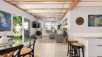 A modern kitchen with a dining area, a TV mounted on the wall, and a view of the garden.