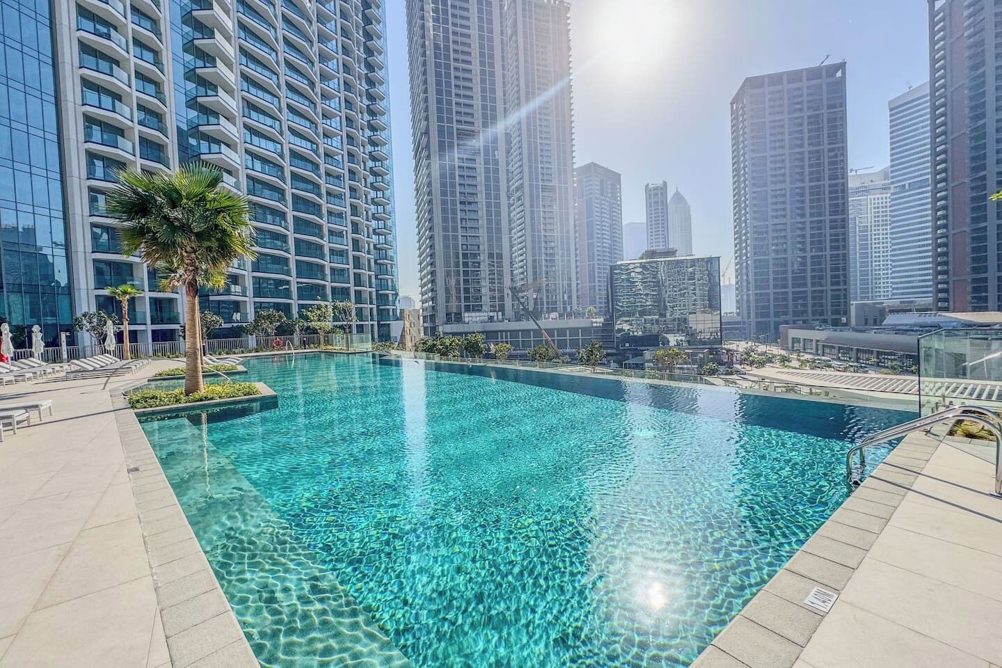Una piscina con agua cristalina, rodeada de edificios altos y palmeras.