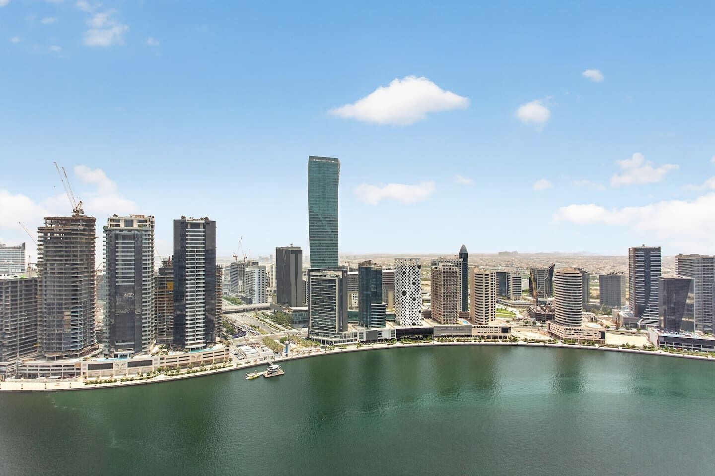 Une vue sur les toits d’une ville, avec des immeubles modernes de grande hauteur, une promenade au bord de l’eau et un ciel dégagé.