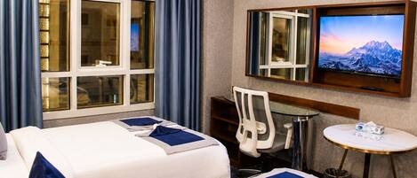 A hotel room with two beds, a desk, a chair, a TV, and a small table with a tissue box.