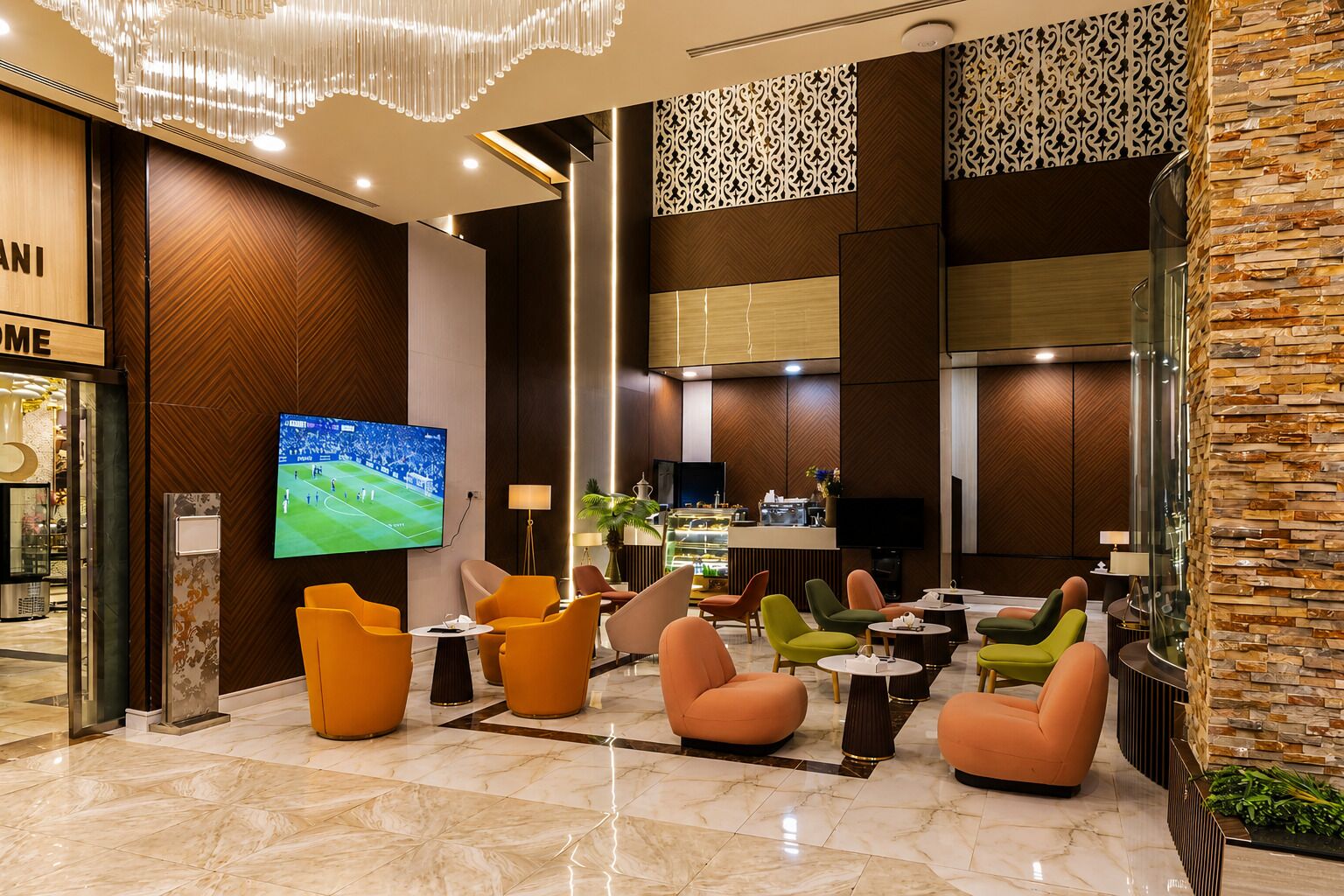 A modern hotel lobby with a large TV, comfortable seating, a bar area, and a decorative wall.