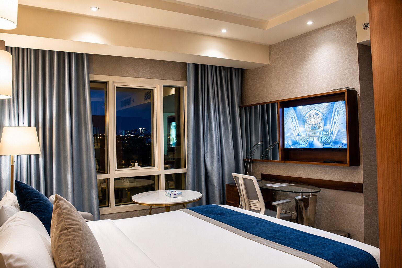 Une chambre d’hôtel avec un lit, un bureau, une chaise, une télévision et une fenêtre avec des rideaux.