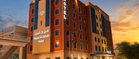 A hotel with a modern design, featuring a prominent sign for 'Nuzul Al Dabab Hotel' and a staircase leading to the entrance.