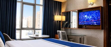 A hotel room with a bed, a desk, a chair, a TV, and a window with curtains.