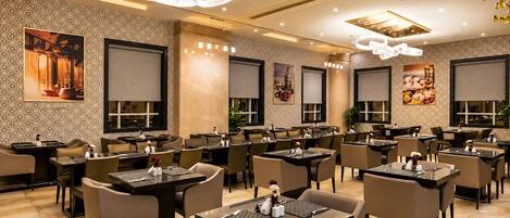 A modern restaurant with multiple dining tables and chairs, decorative wall art, and contemporary lighting fixtures.
