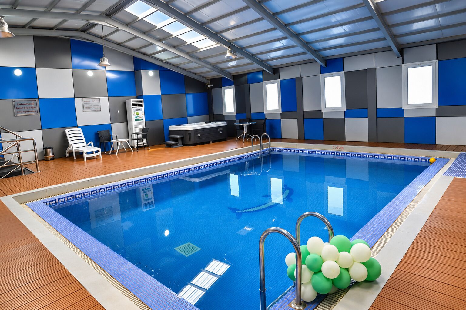 Ein Hallenbad mit einer gefliesten Kante, einem Sprungbrett und einem Liegebereich mit Stühlen.