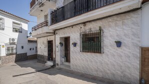 A two-story building with a tiled facade, a balcony with a metal railing, and a small entrance door.
