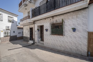 Un bâtiment à deux étages, doté d’une façade recouverte de tuiles, d’un balcon avec une rambarde en métal et d’une petite porte d’entrée.