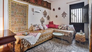 A room with a bed, a small table, a sofa, a decorative tapestry, and a window with bars.